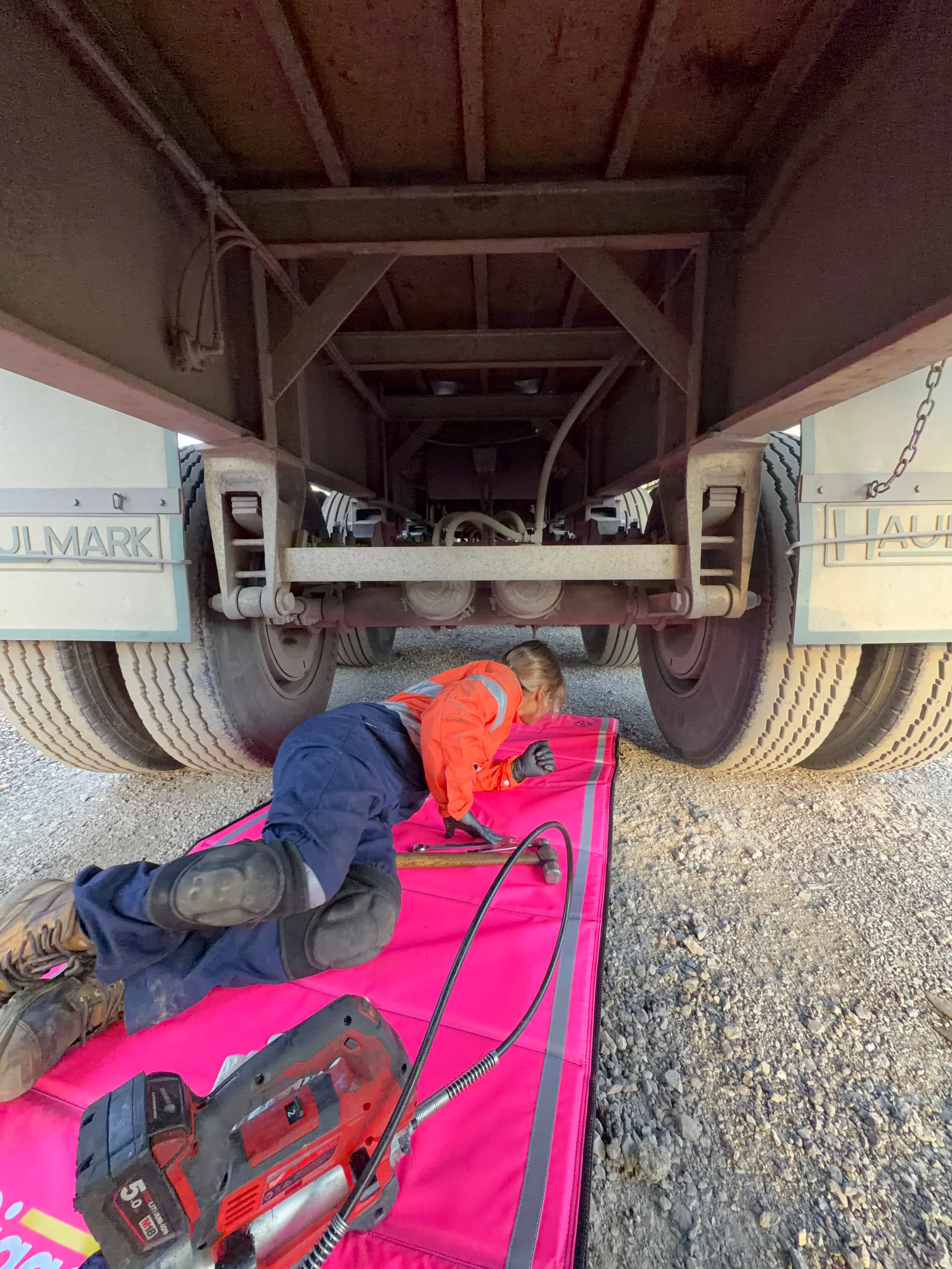 Mechanic in hi-vis working under a truck trailer on a Safety Pink Pro Mat Plus