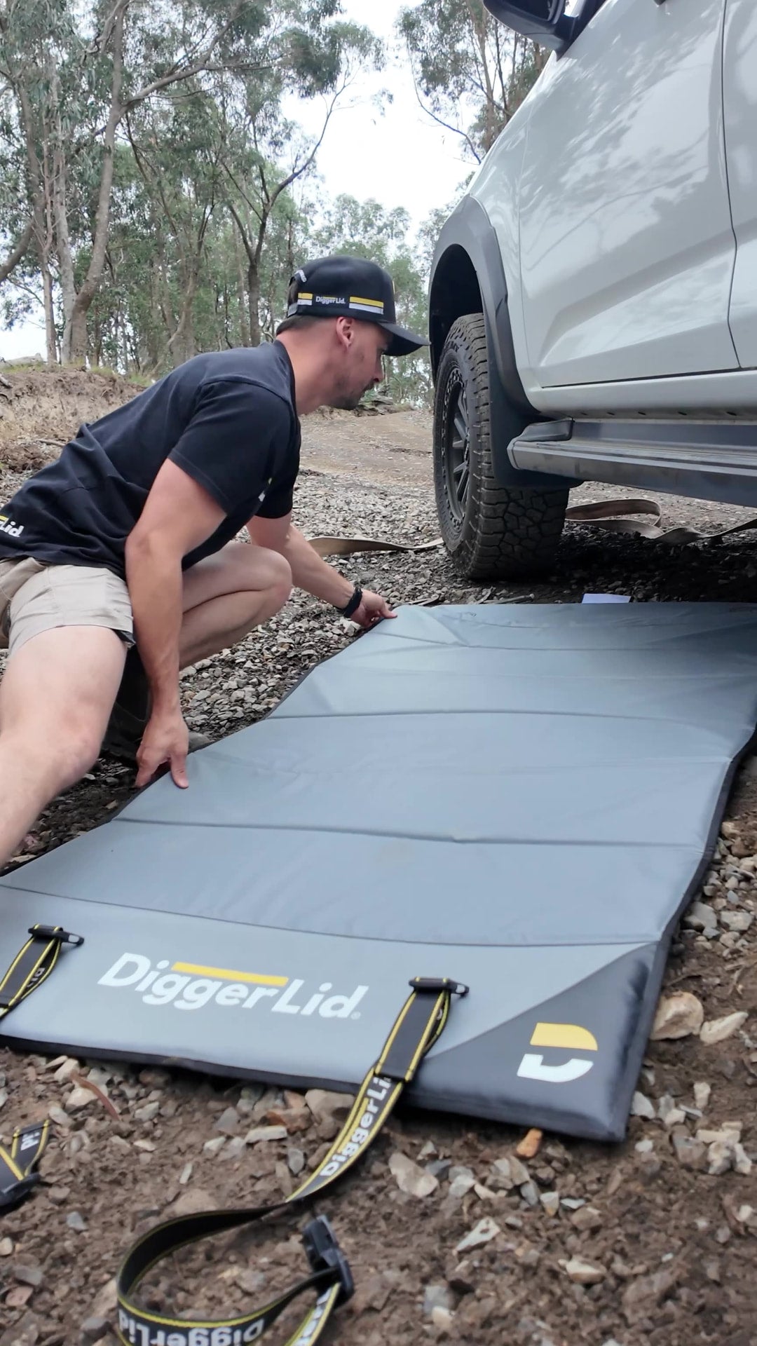 Man rolling out a DiggerLid mat beside a 4WD in the bush